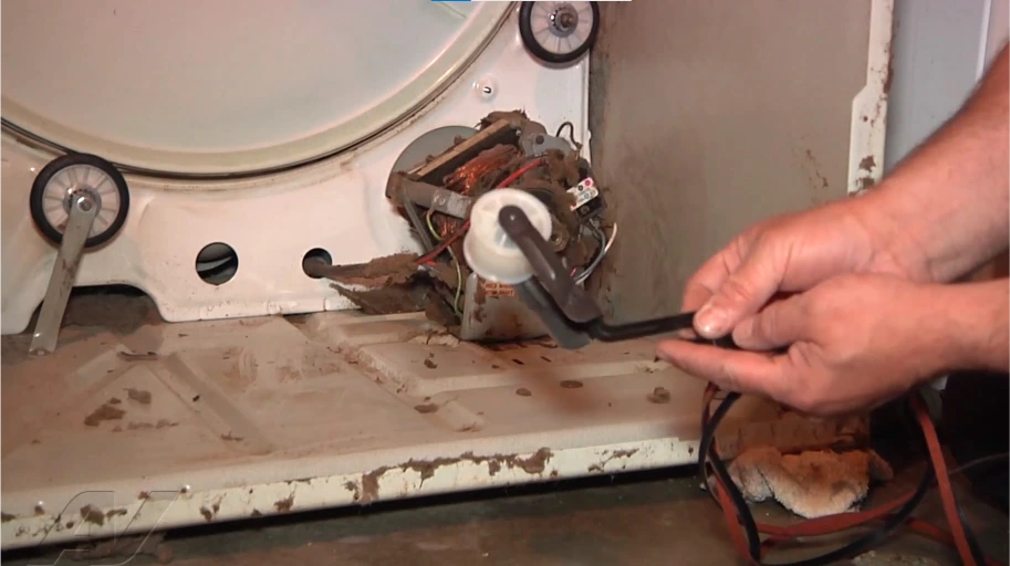 Dryer motor and idler pulley with lint packed around them at the back of an open dryer